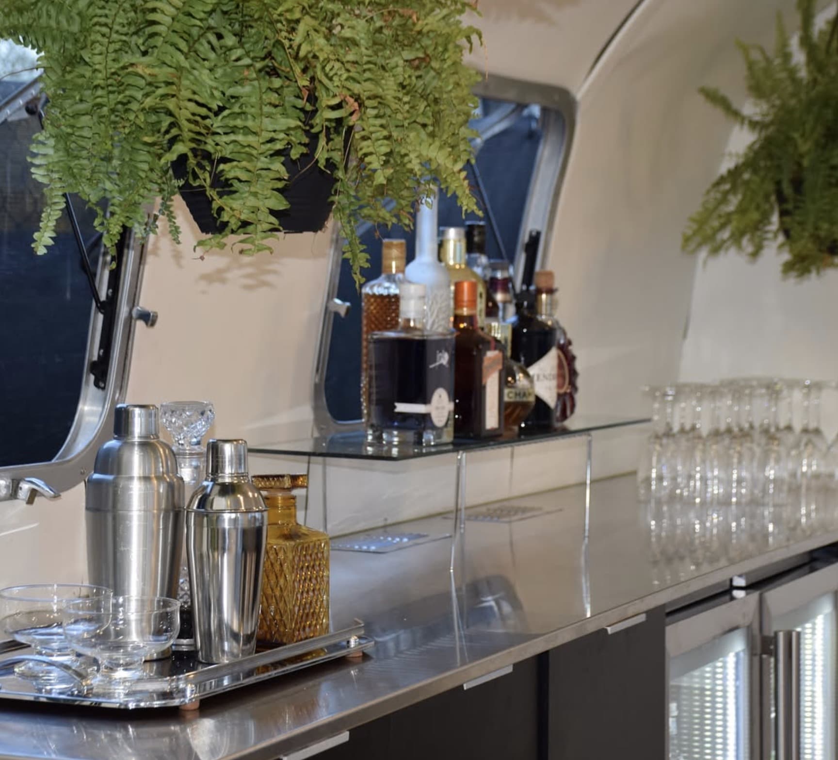 Bar counter detail inside the Airstream with cocktail shakers, amber decanter, glassware and hanging ferns