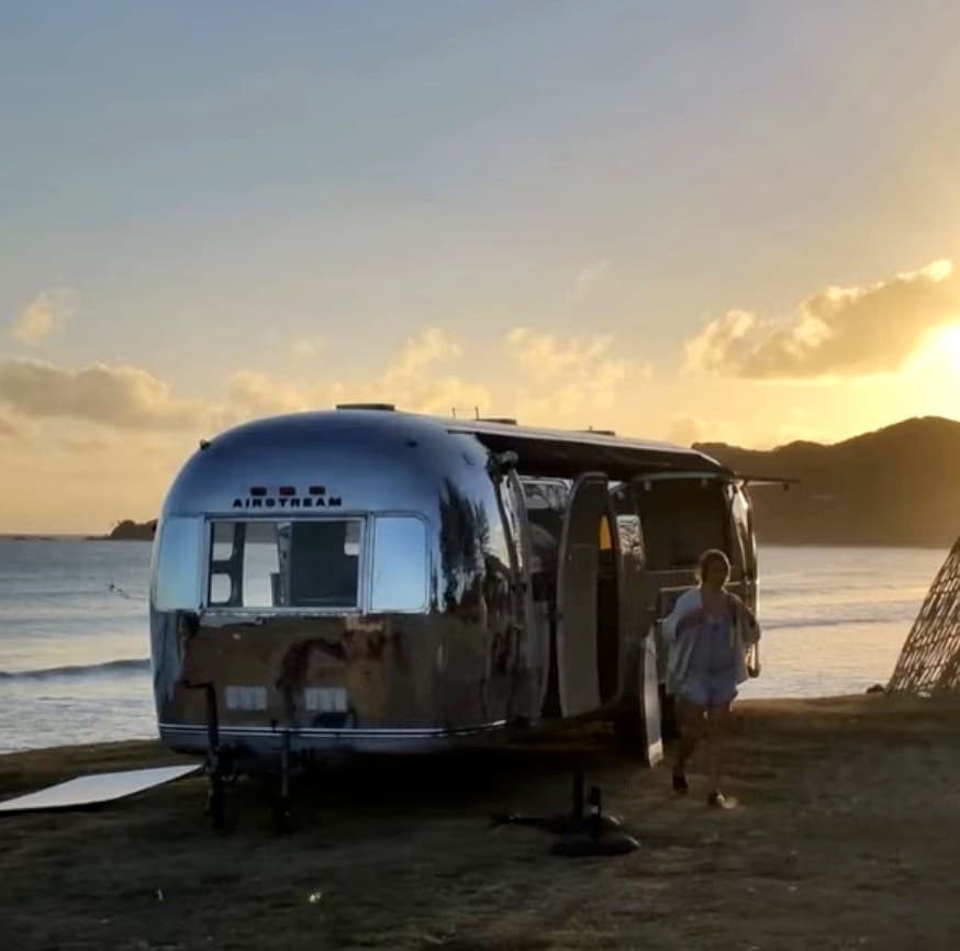 The polished 1972 Airstream parked above the ocean at sunset, door open, golden light on aluminium