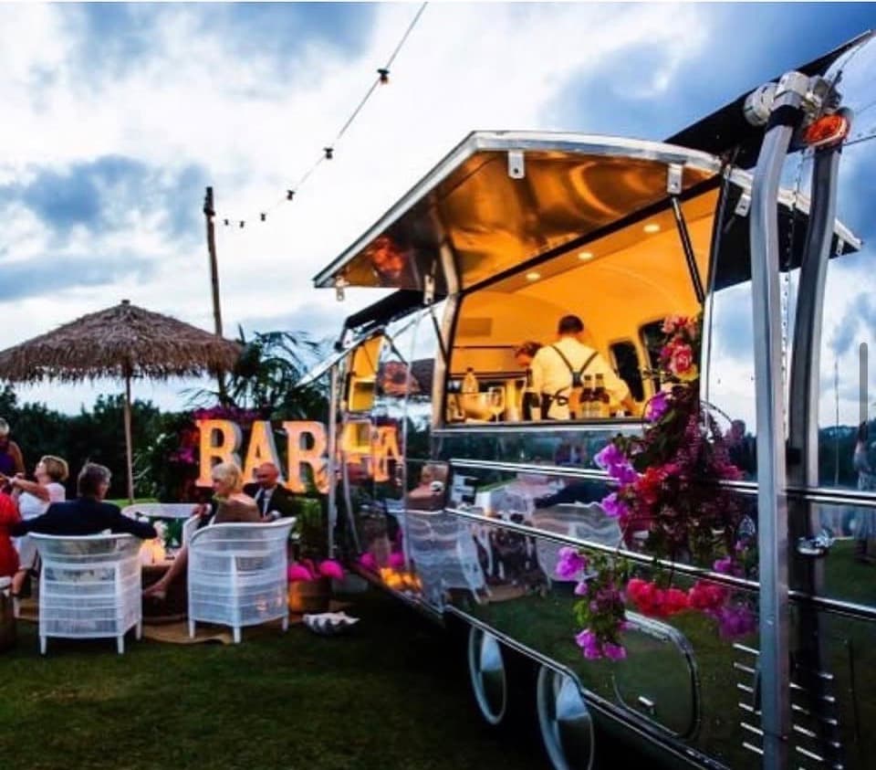The Airstream bar at dusk with illuminated BAR marquee letters, florals and festoon lighting
