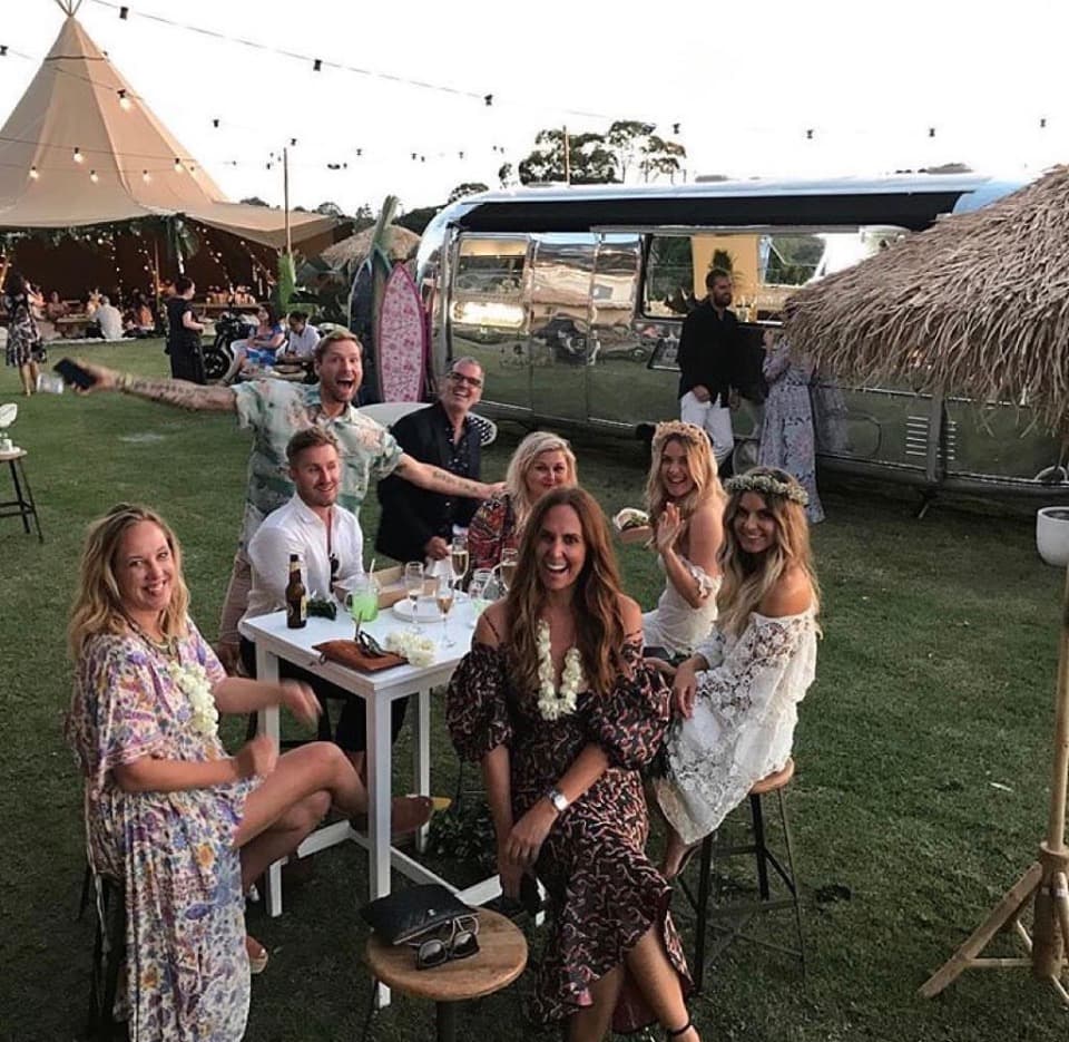 Guests gathered around the Airstream at dusk with festoon lighting