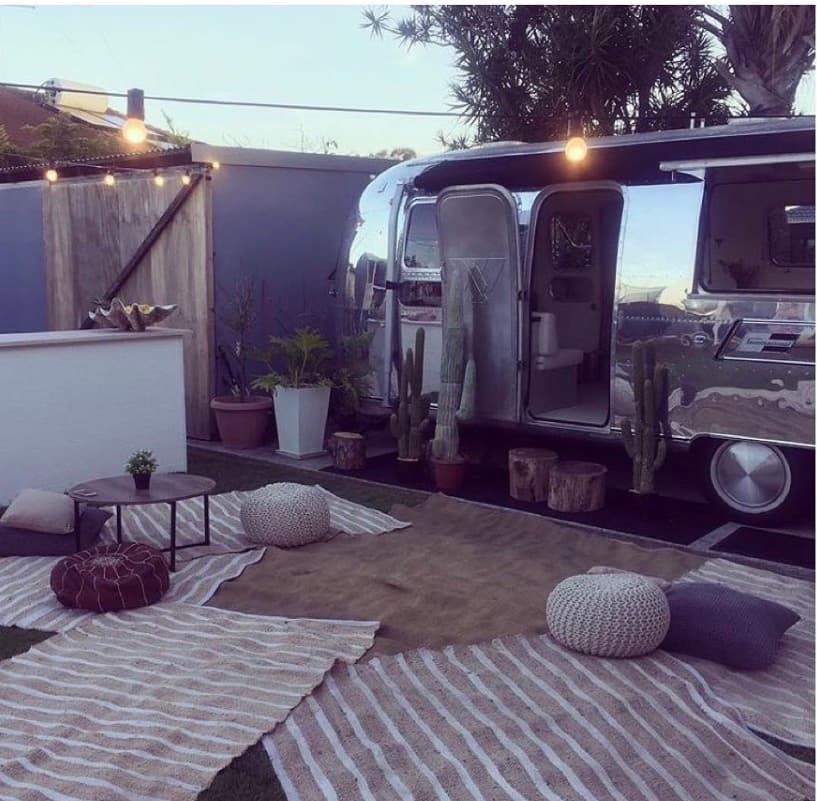 Outdoor lounge beside the Airstream at dusk with rugs, poufs, cactus and festoon lighting