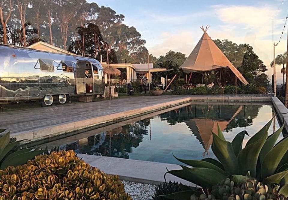 Airstream beside a pool with tipi behind at dusk, framed by agave plants
