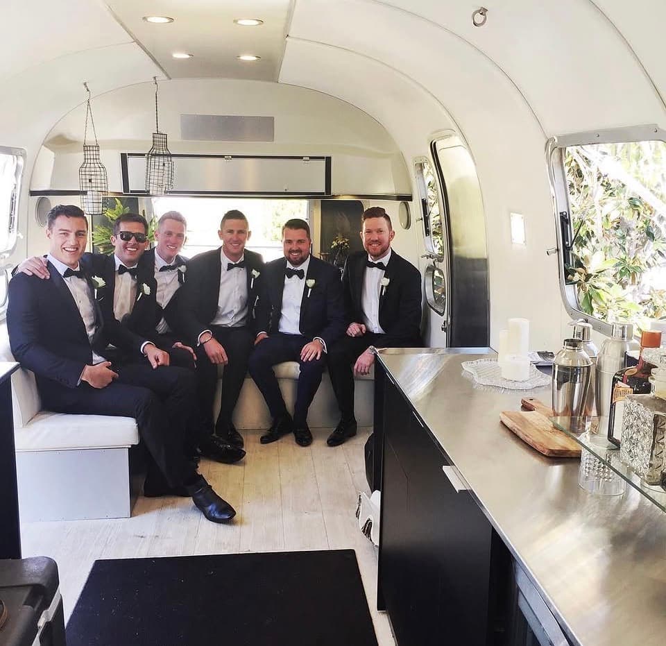 Six groomsmen in tuxedos seated together on the Airstream interior lounge